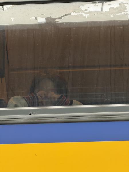 A person sits alone on public transit, looking down with their hand near their face